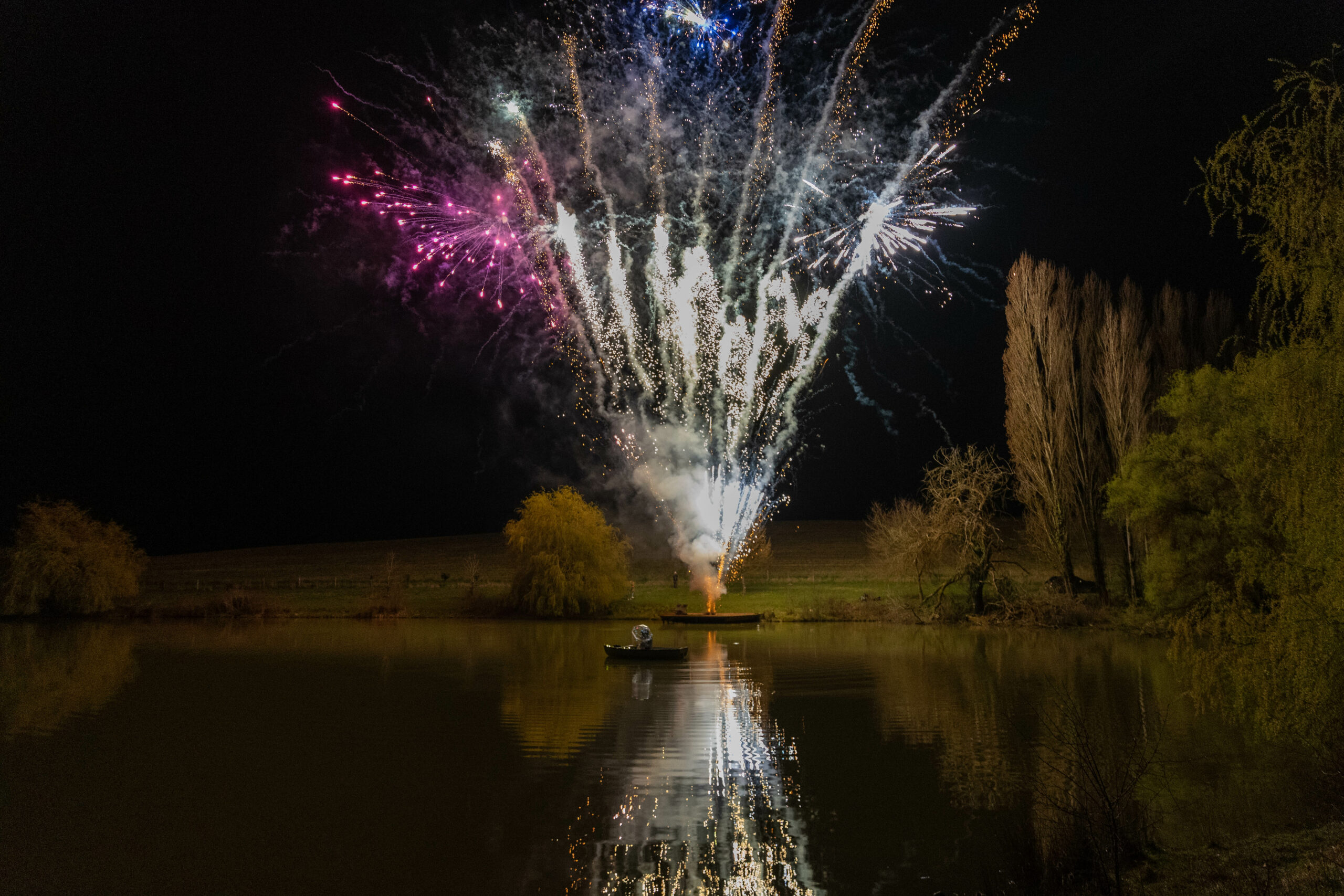 Feu d’artifice illumin-event sur lac calme en occitanie, barque solitaire sous ciel nocturne lumineux