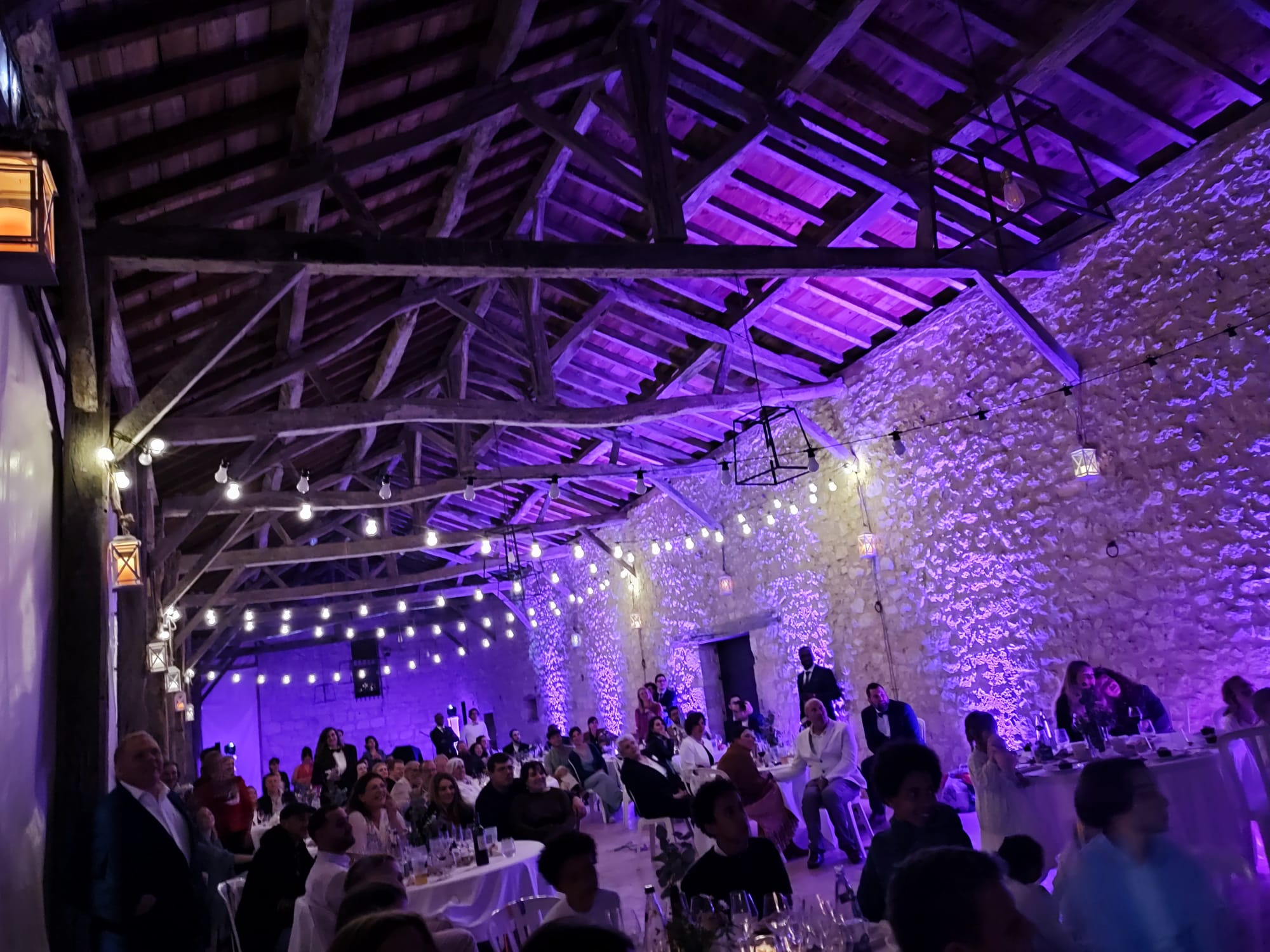 Salle de réception en pierre illuminée en violet par illumin-event pour un mariage festif en Occitanie