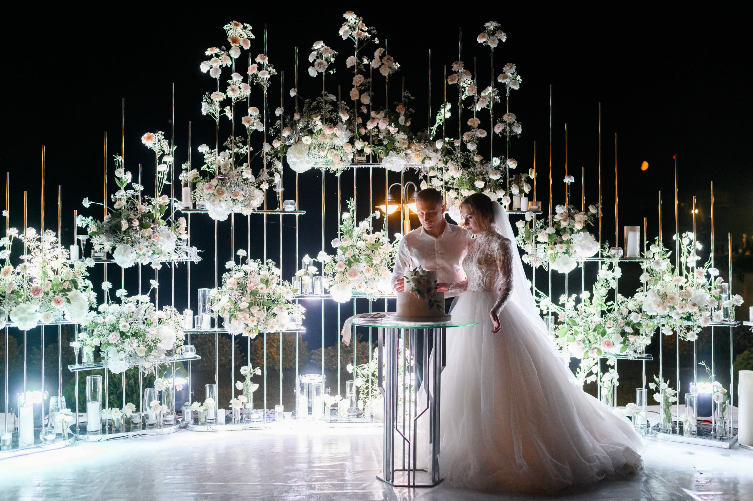 Jeunes mariés coupant leur gâteau de mariage illumin-event sous arche florale romantique en Occitanie